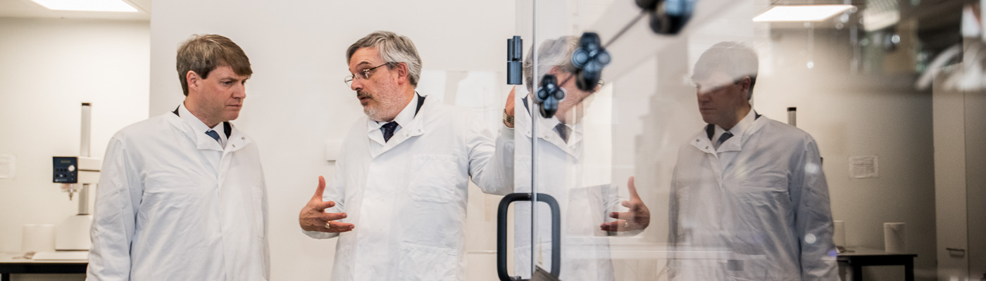 Two male scientists in white lab coats stand chatting.