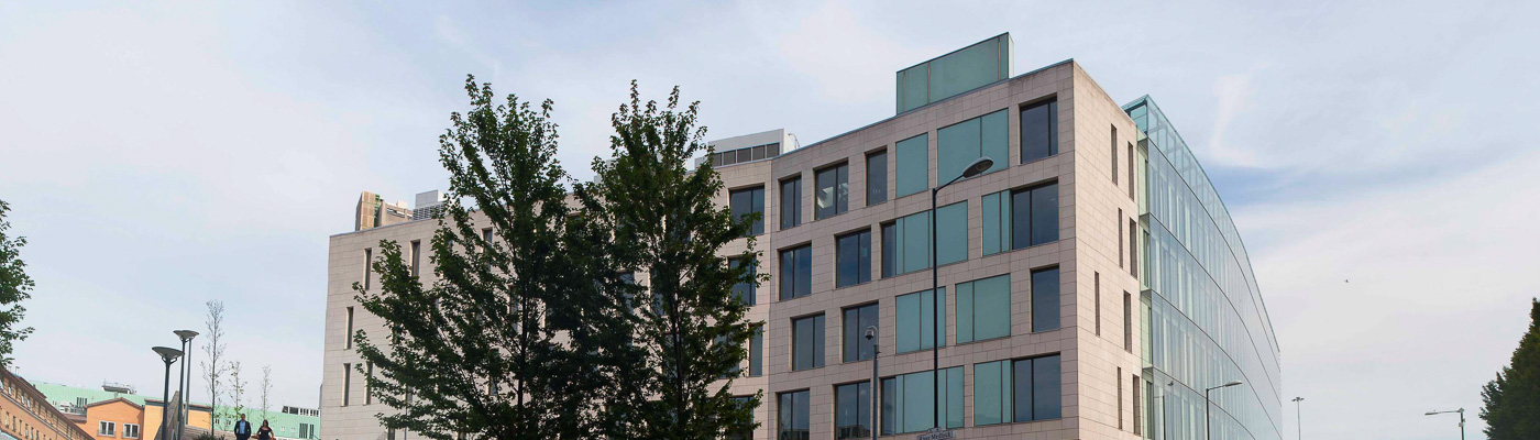 The glass and concrete exterior of the MIB, with a road lined with trees running alongside it.