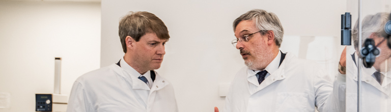 Two male scientists in white lab coats stand chatting.