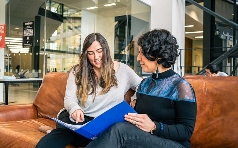 Two women discuss documents in a folio.