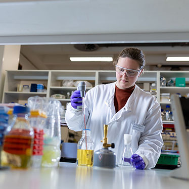 A scientist pipettes liquid into a bottle while standing at a lab bench.