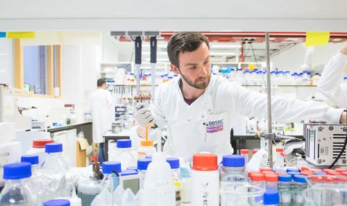 A male scientist in a white lab coat works in a lab.