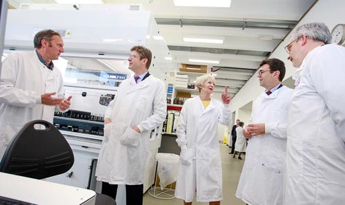 A group of male and female scientists and businesspeople in white coats stand chatting.